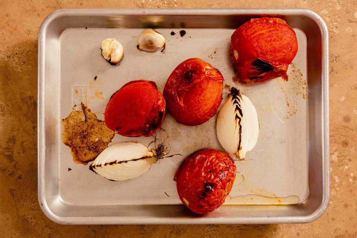 charred tomatoes, onion, and garlic cloves on a baking sheet