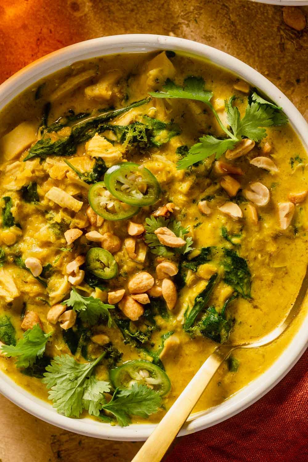 curry lentil soup with chicken in a shallow white bowl topped with cilantro and peanuts