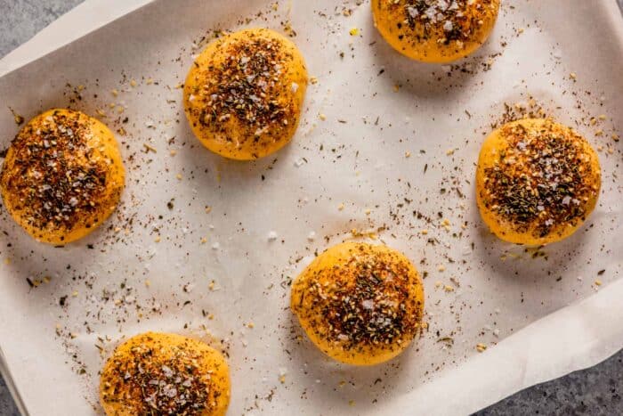 orange-hued dough balls topped with seasoning on a parchment-lined baking sheet