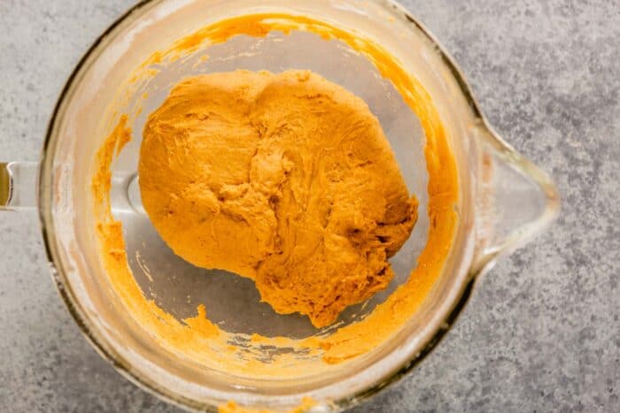 orange-hued dough in a large glass mixing bowl
