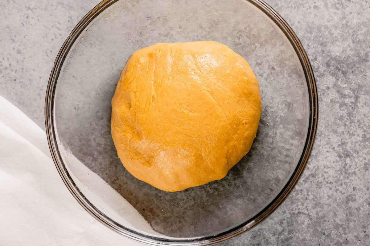 orange-hued dough formed into a ball in a large glass mixing bowl