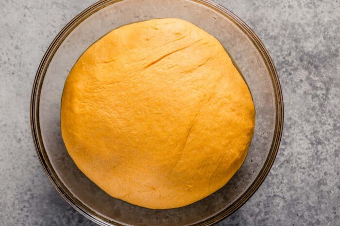 orange-hued dough risen in a large glass mixing bowl