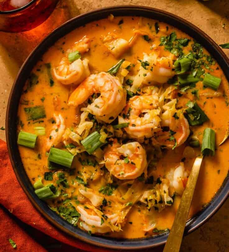 cooked shrimp in an orange-hued broth topped with herbs, lime zest and scallions