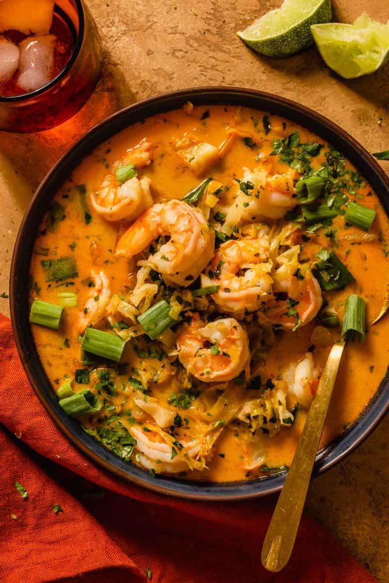 cooked shrimp in an orange-hued broth topped with herbs, lime zest and scallions