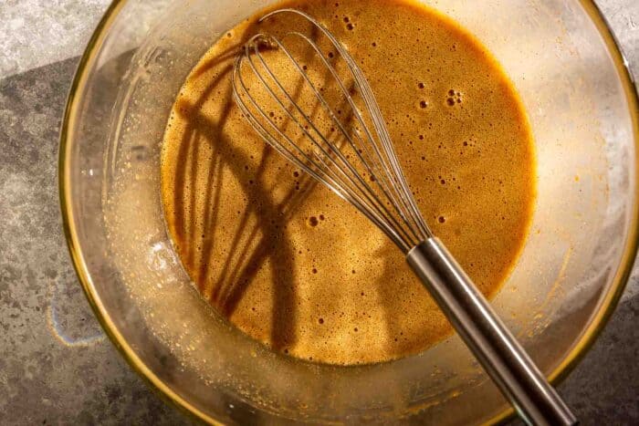 foamy brown batter in a large glass bowl with a metal whisk set in it
