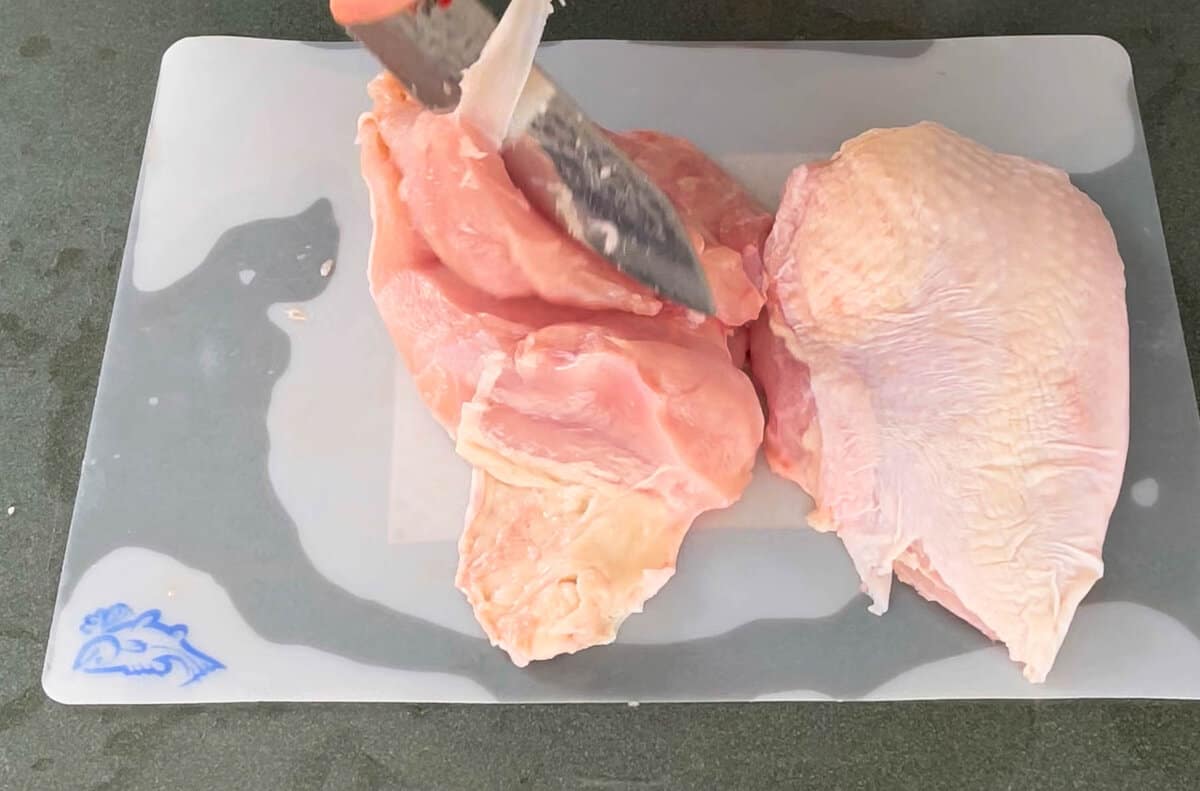 a set of hands breaking down a raw turkey with a chefs knife on a plastic cutting board