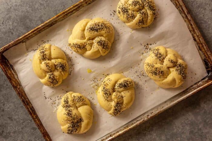 knotted dough rolls on a parchment-lined baking sheet topped with poppy seeds and sesame seeds