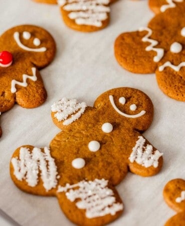 gingerbread cookie cut outs on parchment paper, decorated with icing, sprinkles and red hot candies