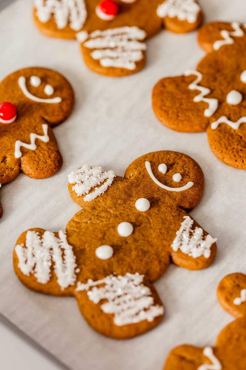 gingerbread cookie cut outs on parchment paper, decorated with icing, sprinkles and red hot candies