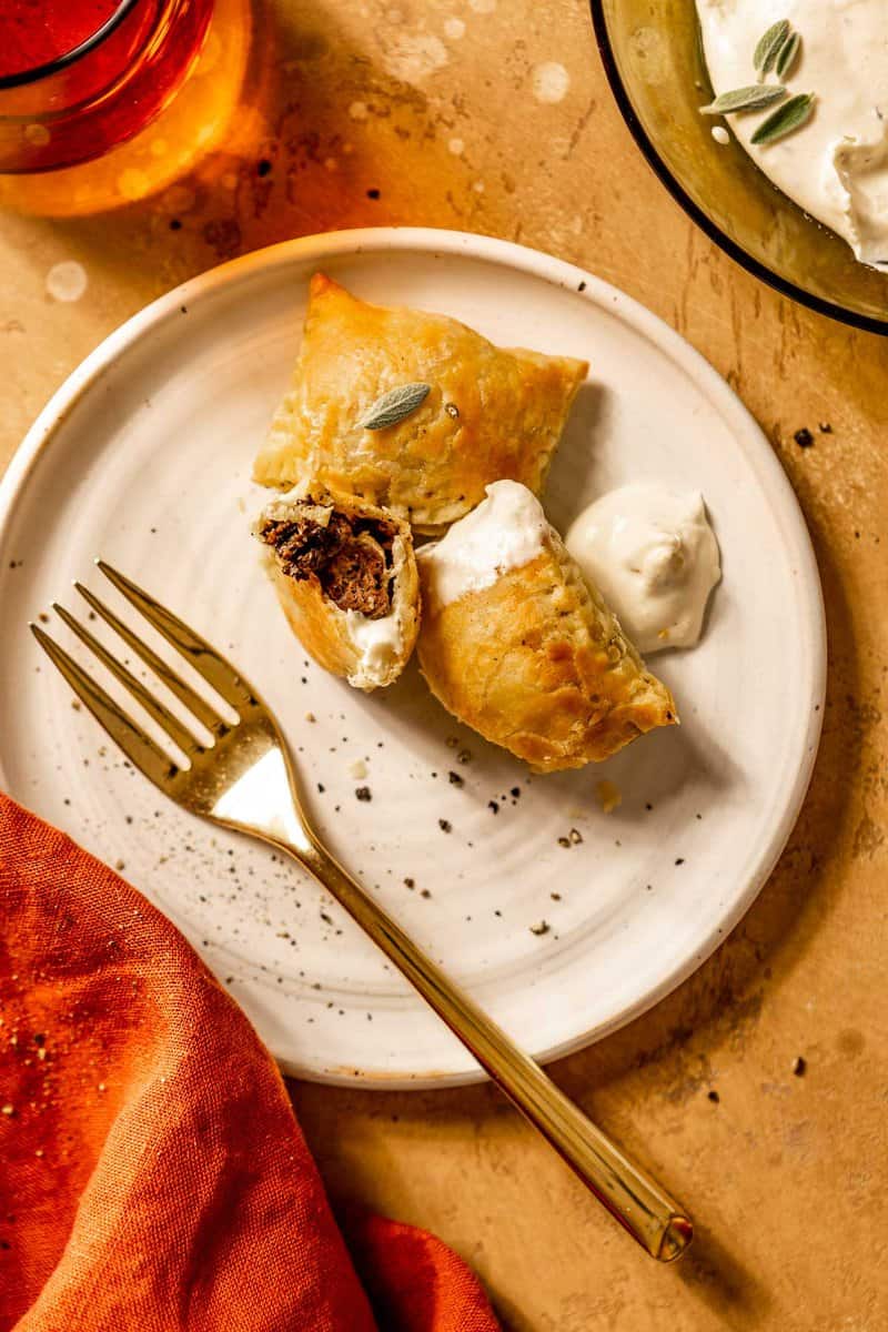 three mini beef wellington bites set on a white plate with a gold fork and white sauce