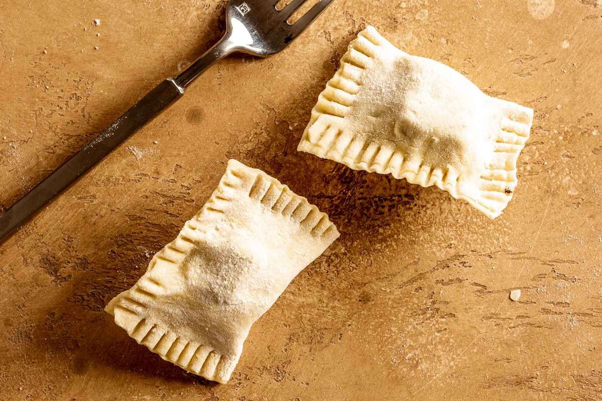 two ravioli-like dough pockets on a counter wit a fork