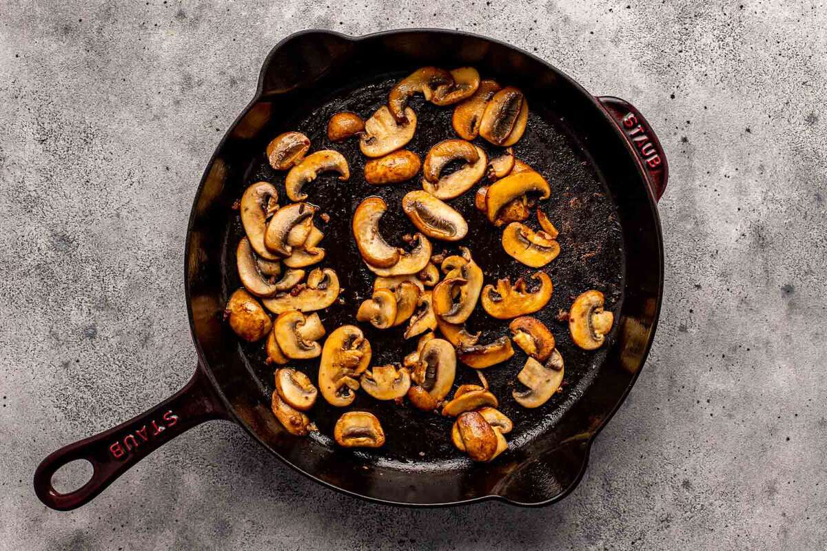 sliced mushrooms cooking in a cast-iron skillet