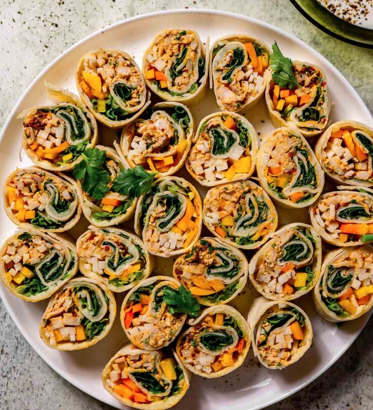 large white plate filled with small mexican roll ups filled with veggies, herbs and chicken