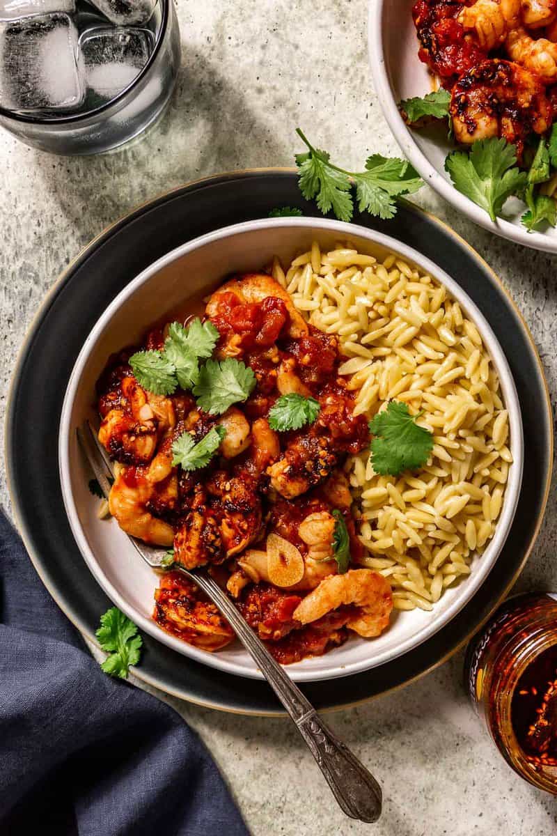 fresh cilantro, chili crisp, and shrimp in a spicy tomato sauce served over orzo pasta in a shallow white bowl