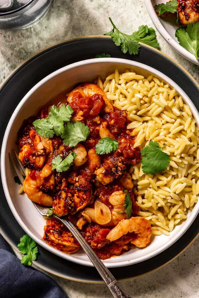fresh cilantro, chili crisp, and shrimp in a spicy tomato sauce served over orzo pasta in a shallow white bowl
