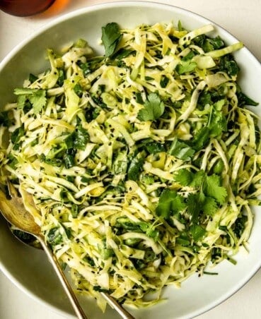 shredded green cabbage salad in a large white bowl with herbs and sesame seeds