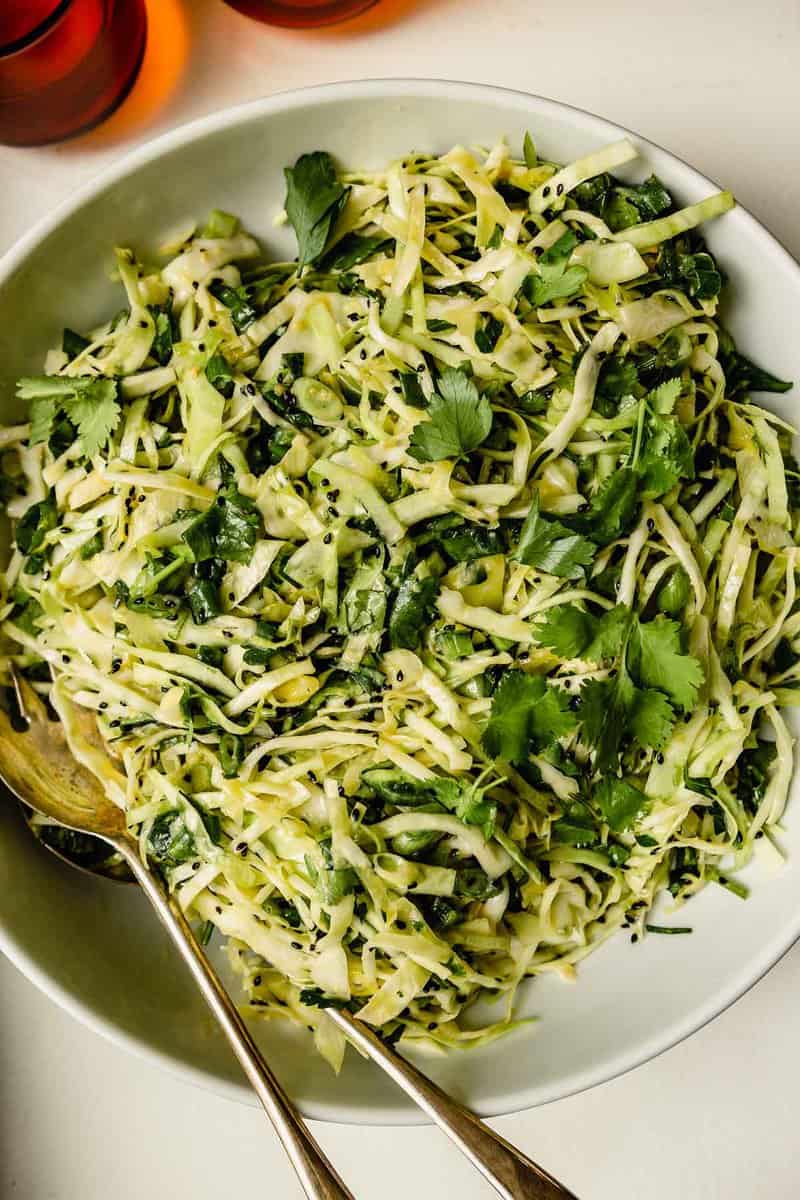 shredded green cabbage salad in a large white bowl with herbs and sesame seeds
