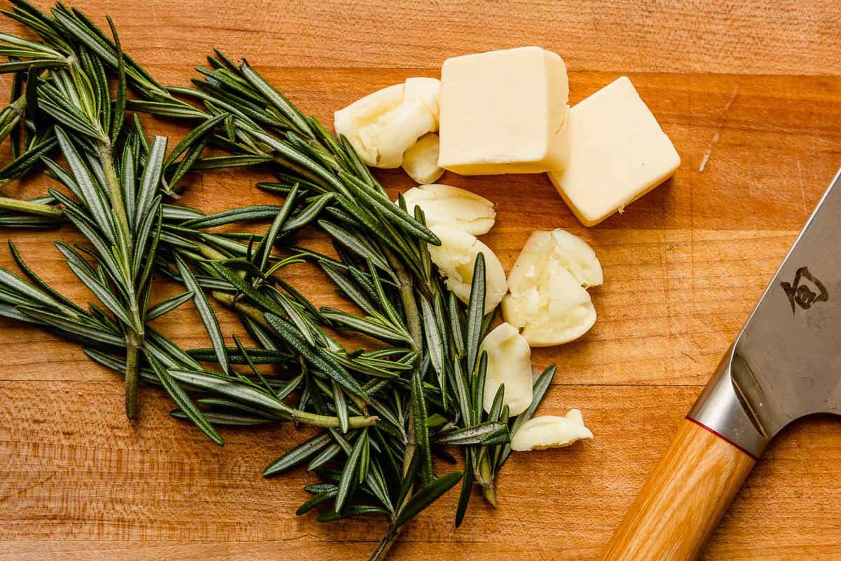 butter, garlic cloves, and rosemary on a wood cutting board