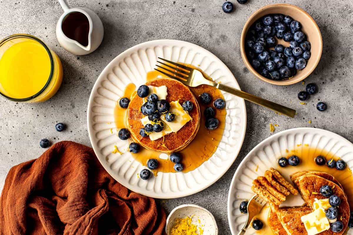 pancakes on a white plate topped with blueberries, butter and maple syrup