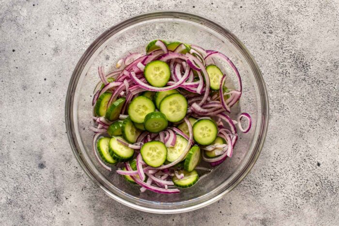cucumbers and red onion in a glass bowl with vinegar