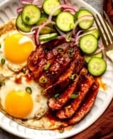 sliced steak, fried eggs, and cucumbers on a plate with orange napkins and glassware set around it