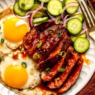 sliced steak, fried eggs, and cucumbers on a plate with orange napkins and glassware set around it