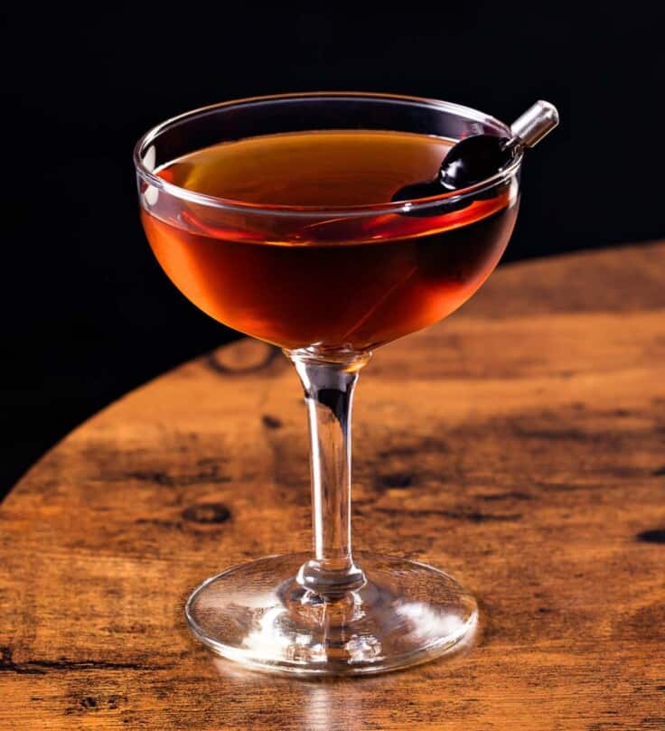 manhattan cocktail in a coupe glass set on a wood table with a cherry as a garnish