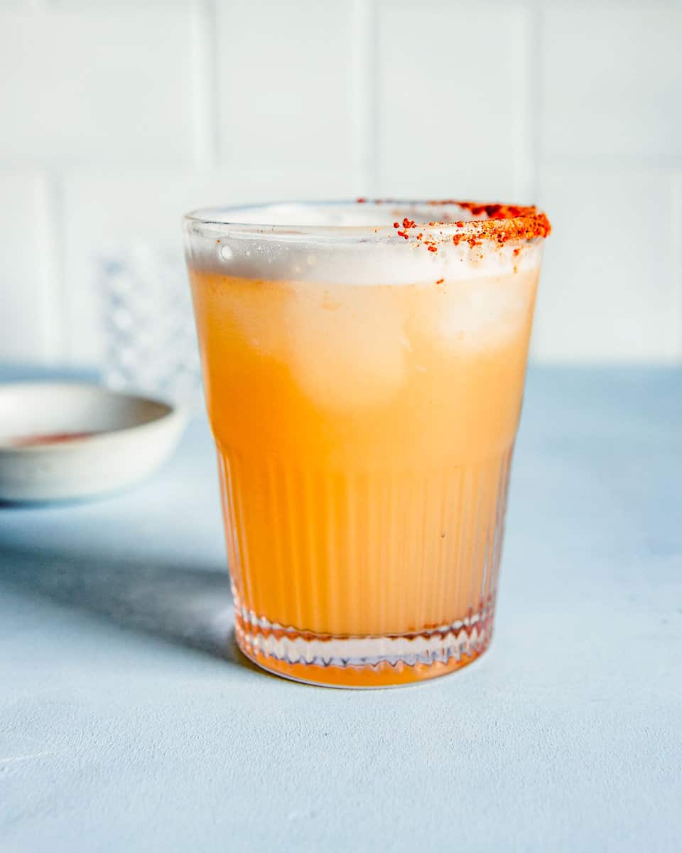 paloma cocktail in a glass rimmed with red spice set on a blue counter