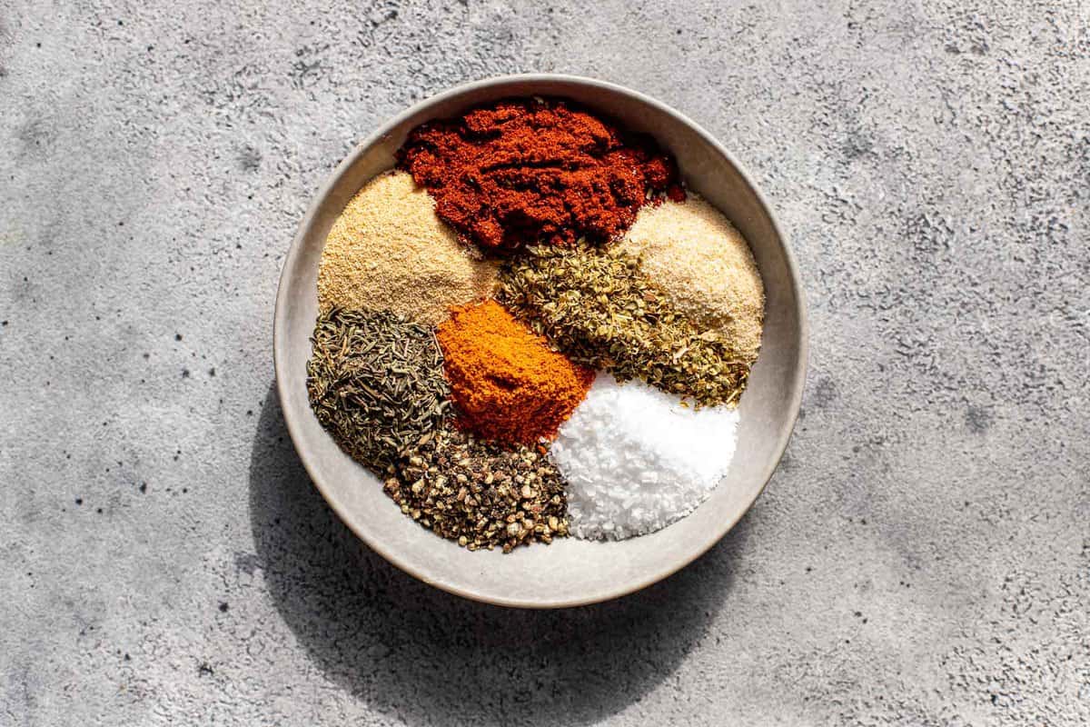 a mix of spices and dried herbs in small piles in a medium shallow white bowl