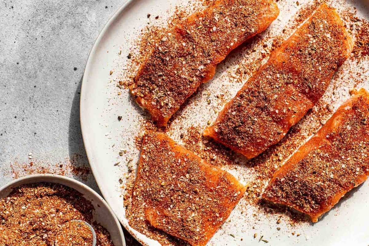blackening spice blend on raw salmon fillets on a large white plate