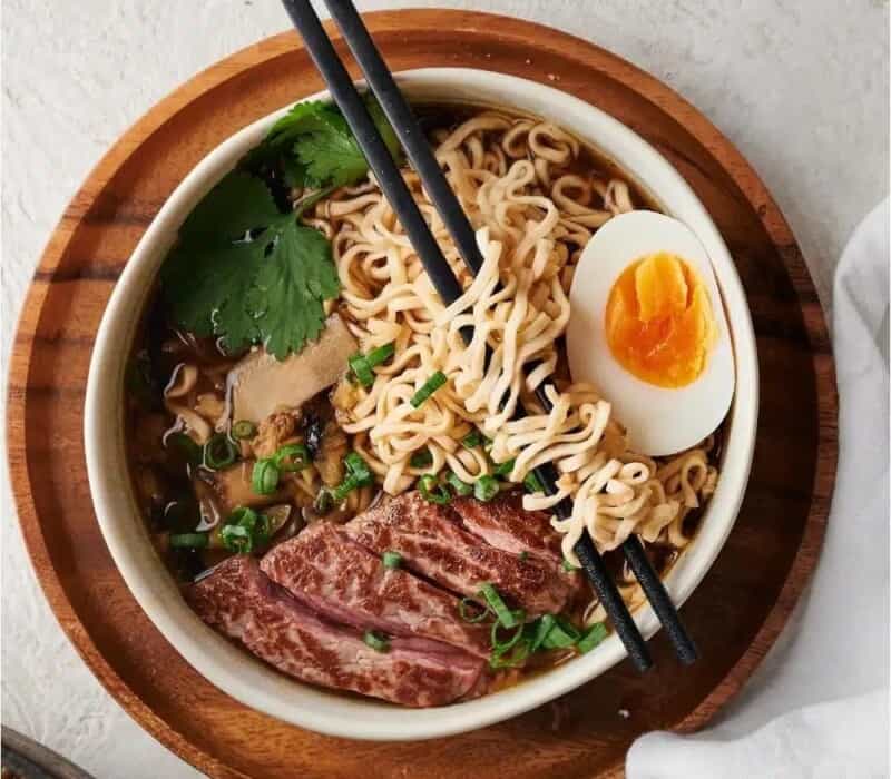 bowl of ramen topped with sliced steak, soft boiled egg and scallions