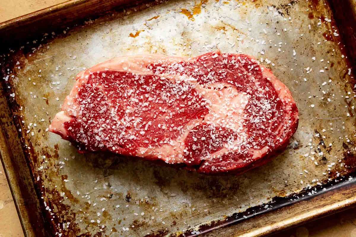 raw steak seasoned with salt set on a baking sheet