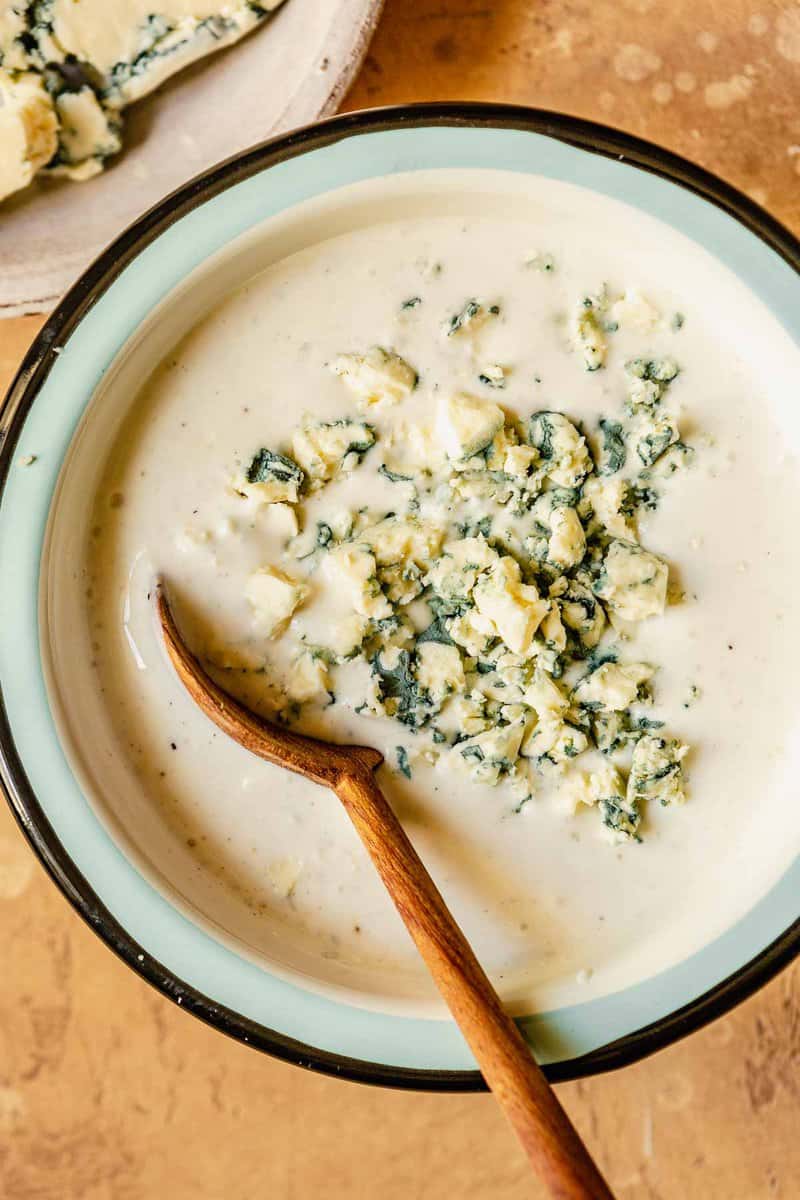 creamy blue cheese dressing in a blue and white metal bowl with a wooden spoon set in it