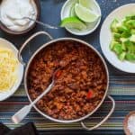 pot of chili on a blue table with toppings set around it in small bowls