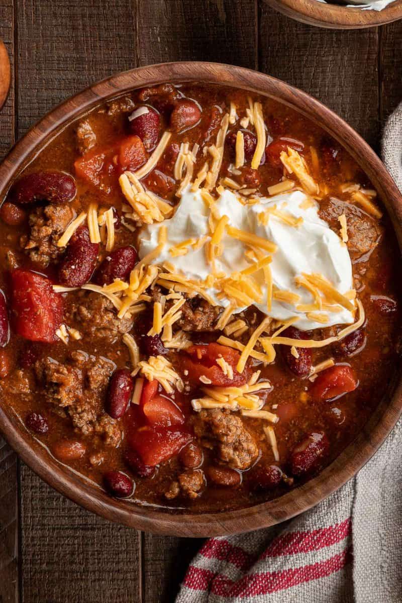 chili in a brown bowl topped with sour cream and shredded cheese