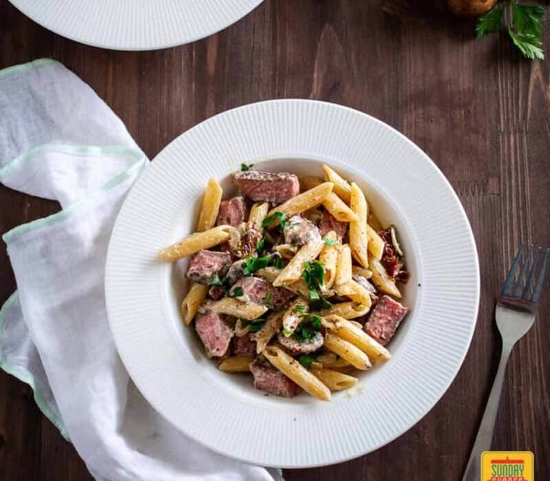 penne pasta with steak in a shallow white bowl