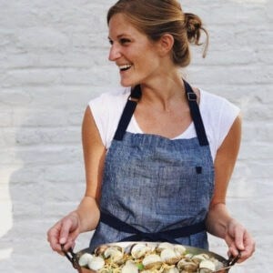 blonde woman in a blue apron holding a pan