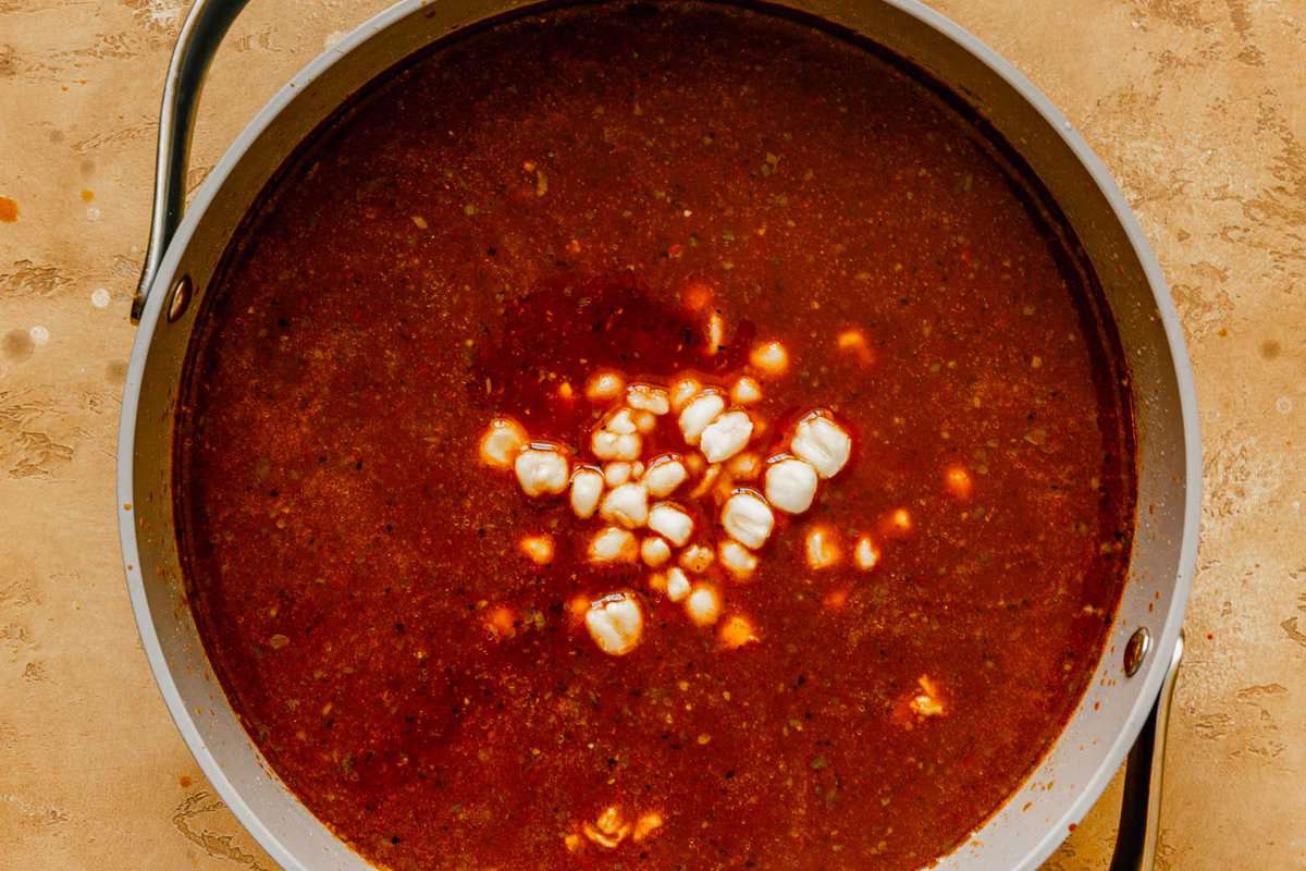 bright red soup in a large pot with white hominy