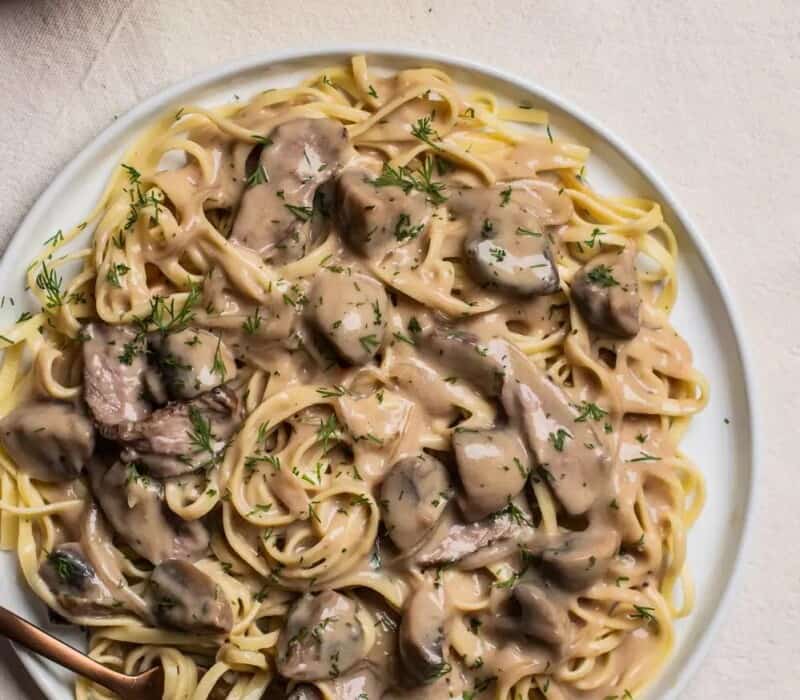 beef stroganoff over noodles on a large white plate