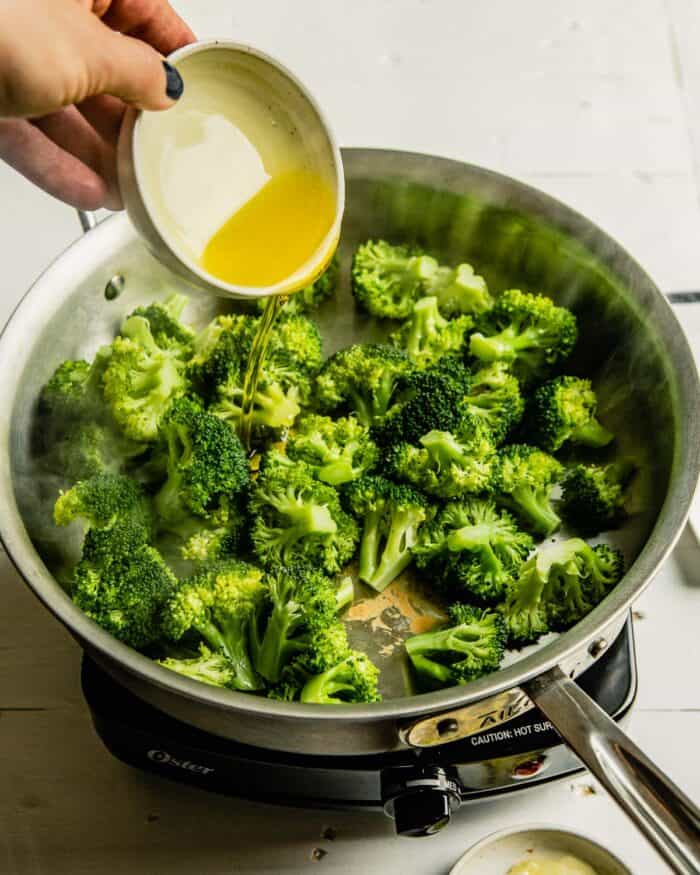 oil being added to a saute pan filled with broccoli florets 