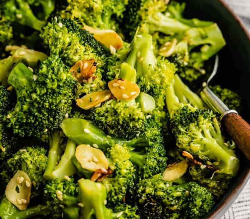 sautéed broccoli in a shallow blue bowl with a wooden-handled spoon