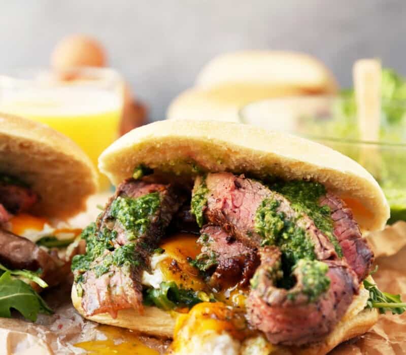 sliced steak piled onto a ciabatta roll with an over easy egg and green herb sauce