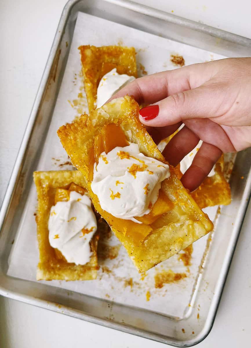 mango puff pastry tart topped with whipped cream and orange zest