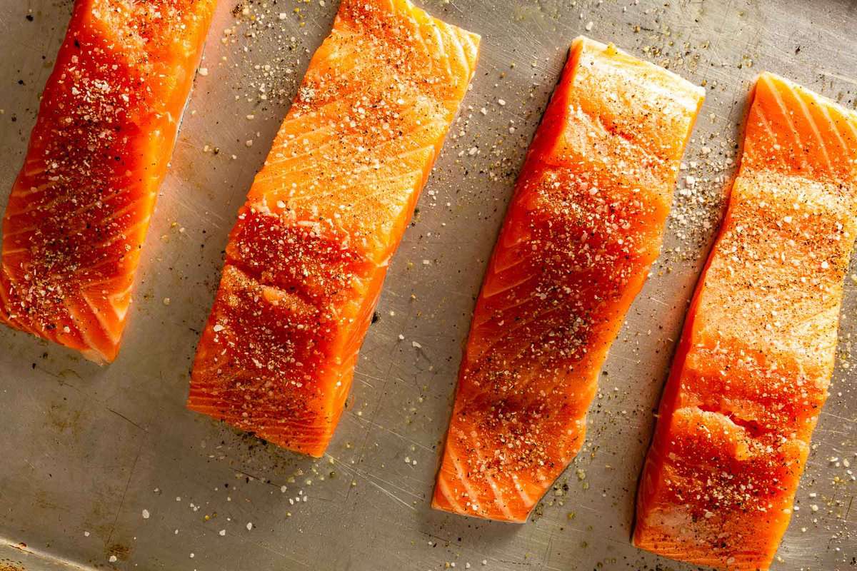 raw salmon fillets on a baking sheet with salt and pepper