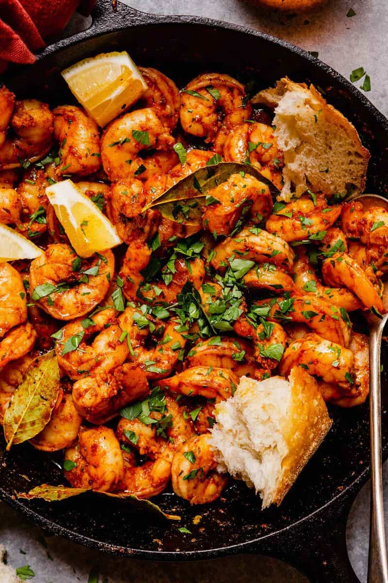 spiced shrimp in a cast-iron skillet with hunks of bread, lemon wedges and chopped parsley