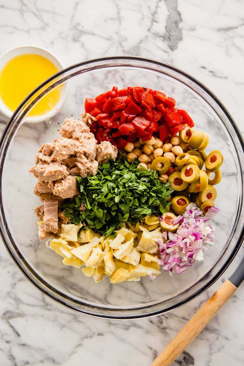 tuna, olives, artichokes, onions, red peppers and parsley in a large glass bowl
