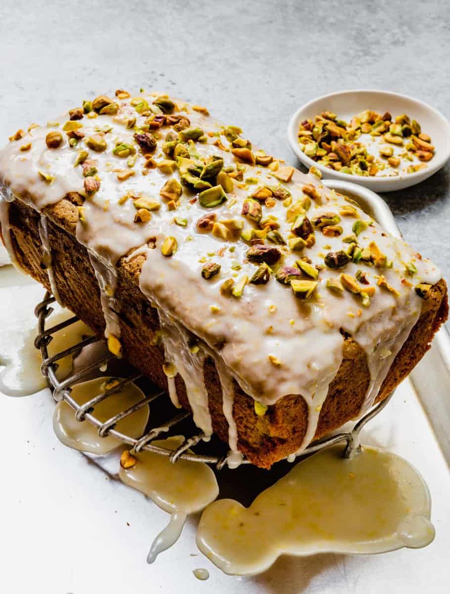 pistachio cake on a wire rack with glaze dripping down it and chopped pistachios on top