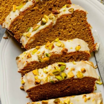 slices of iced pistachio cake on a large white platter topped with chopped pistachios