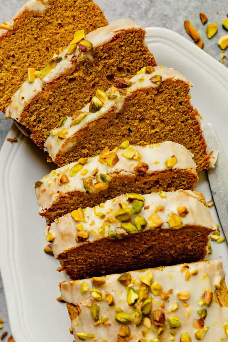 slices of iced pistachio cake on a large white platter topped with chopped pistachios