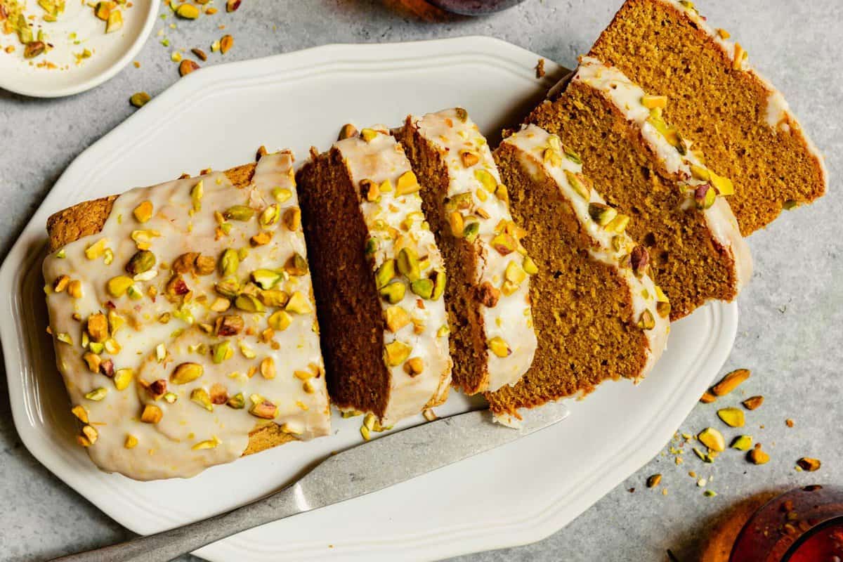 slices of iced pistachio cake on a large white platter topped with chopped pistachios